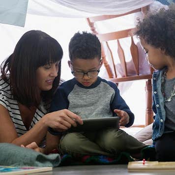Mother reading to her sons, under a blanket fort | Hero Images/Getty Images