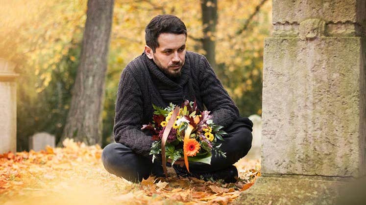 Man mourning loved one at graveyard | ajkkafe/Getty Images