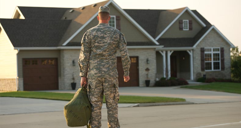 Military man wearing fatigues standing outside of his home