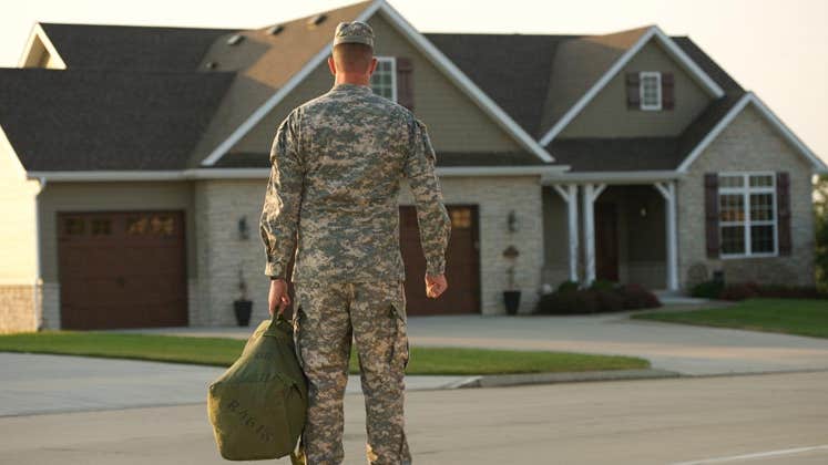 Military man wearing fatigues standing outside of his home
