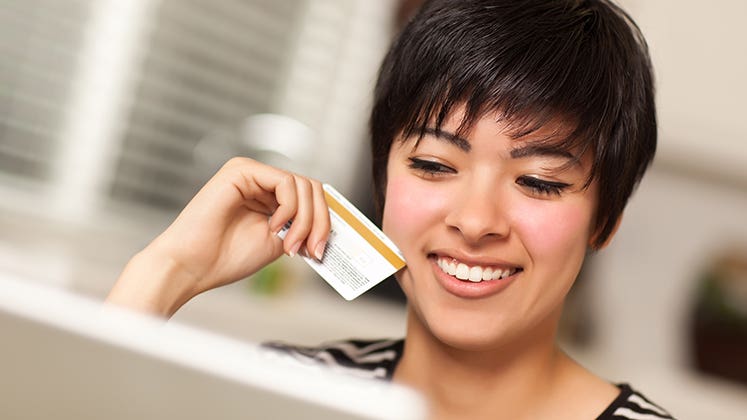 Smiling woman holding credit card while using laptop © Andy Dean Photography/Shutterstock.com