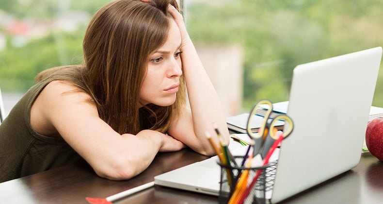 Woman slumped over her desk looking at laptop © iStock