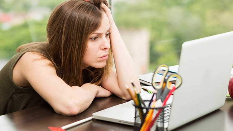 Woman slumped over her desk looking at laptop © iStock