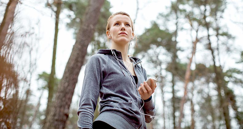 Woman holding mp3 player, running in the woods | Luis Alvarez/DigitalVision/Getty Images
