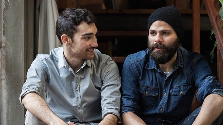 Two male friends sitting together in staircase | iStock.com/lorenzoantonucci