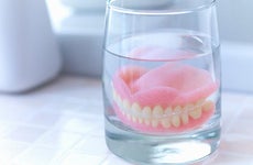 Dentures soaking on glass | Adam Gault/Getty Images