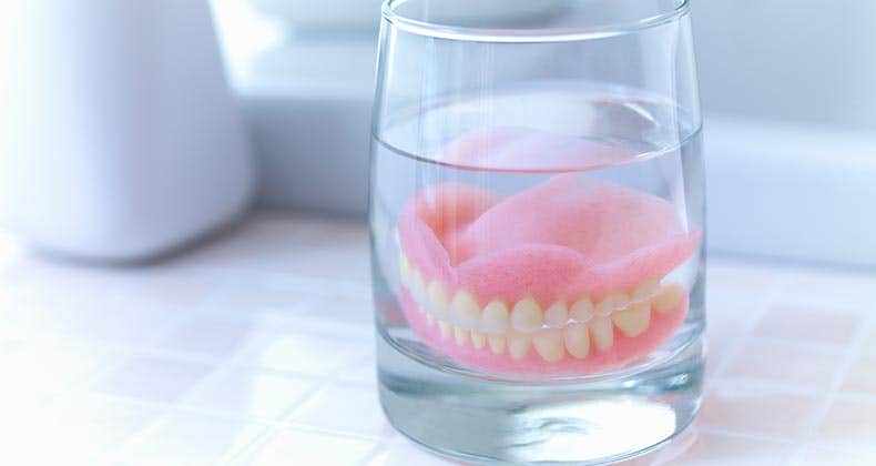 Dentures soaking on glass | Adam Gault/Getty Images
