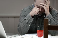 Stressed man in dining room overwhelmed with debt © iStock
