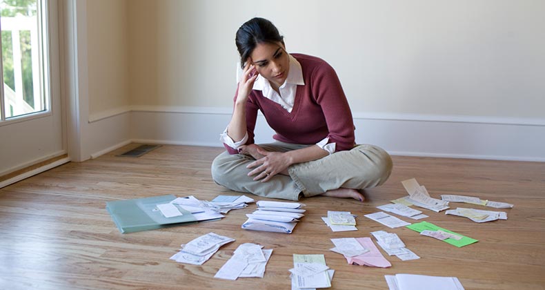 Young woman sitting on floor staring at bills | iStock.com/LifesizeImages
