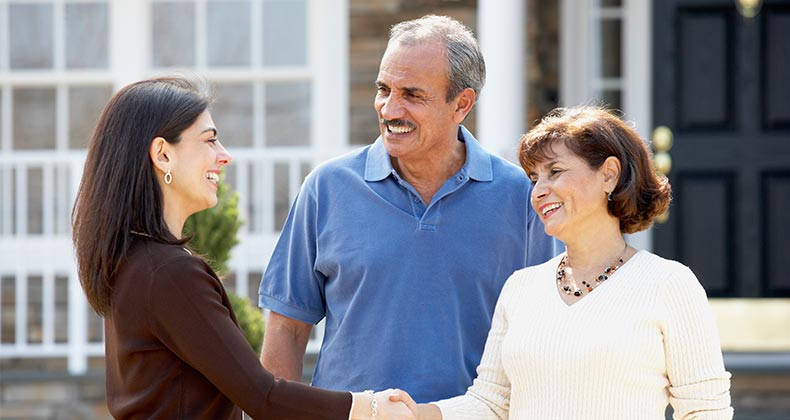 Mature couple shaking hands with real estate agent in front of house | Ariel Skelley/Getty Images
