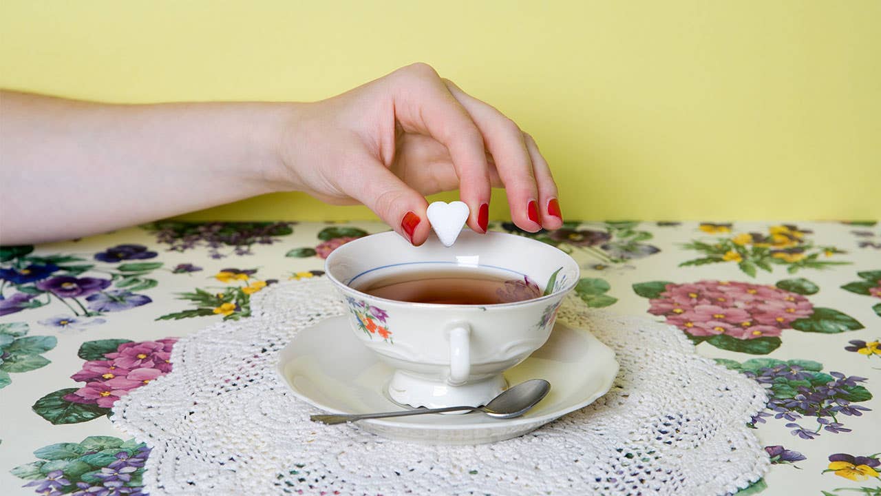 Woman dropping sugar cube into tea