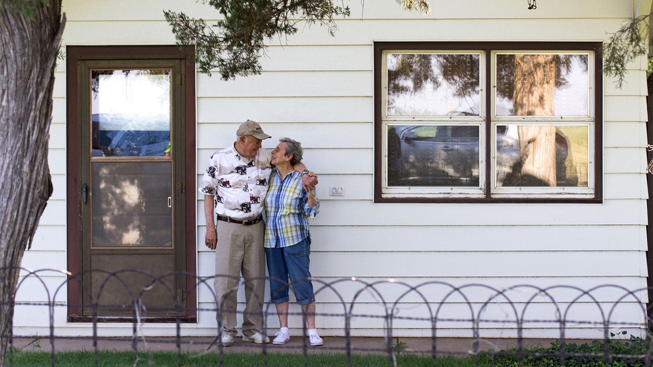 Older couple stand in front of house