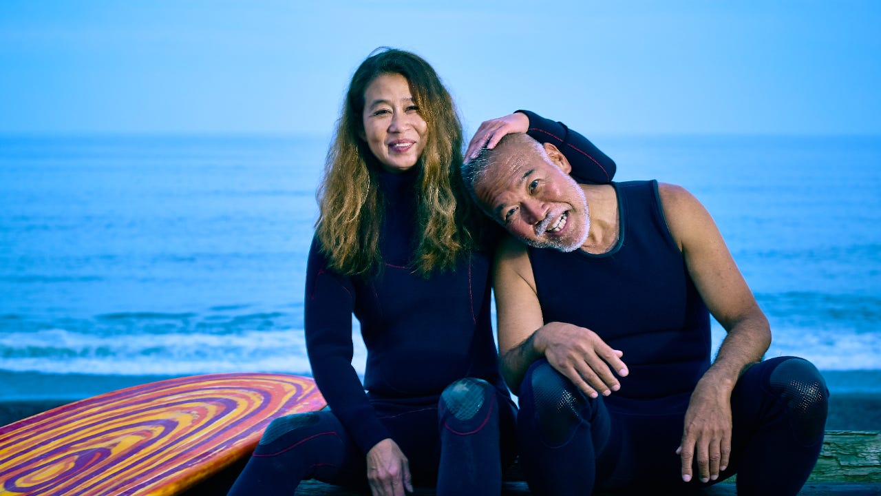 An older surfer couple hug at the beach