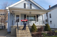 Woman holds up sold sign at new home