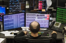 A stock trader sits in front of multiple trading screens