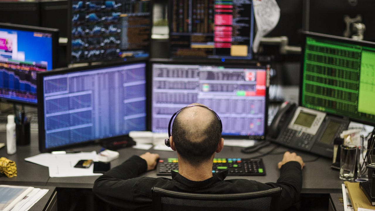 A stock trader sits in front of multiple trading screens