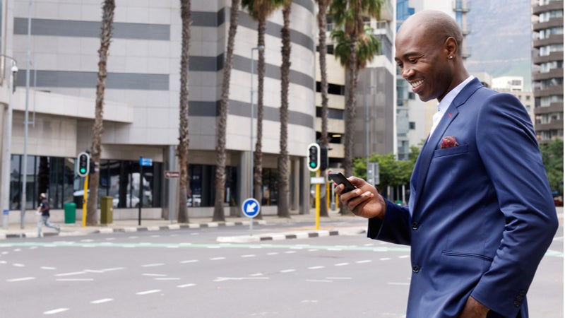 African American businessman smiling at cell phone while walking in the city