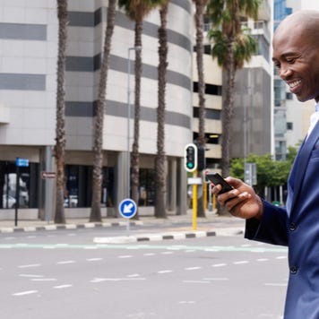 African American businessman smiling at cell phone while walking in the city