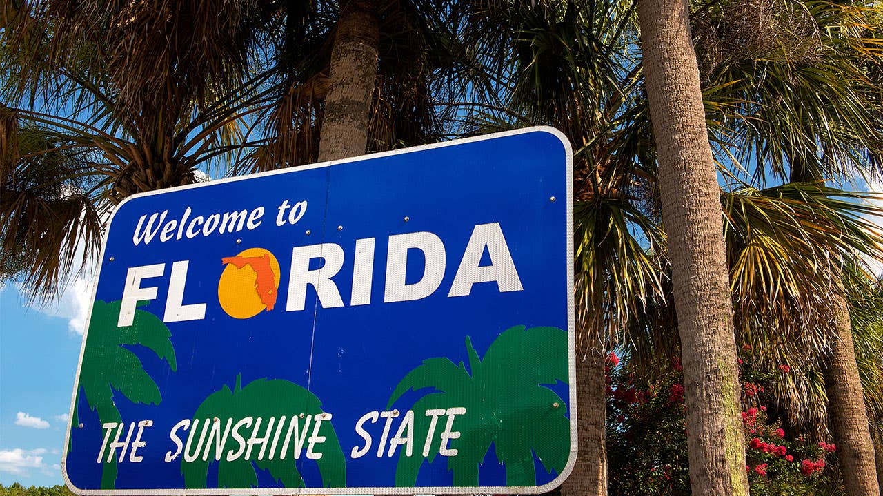 A "Welcome to Florida" sign stands in front of a palm tree