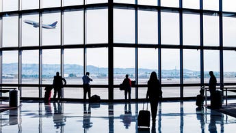 Silhouettes of passengers waiting at an airport in front of window