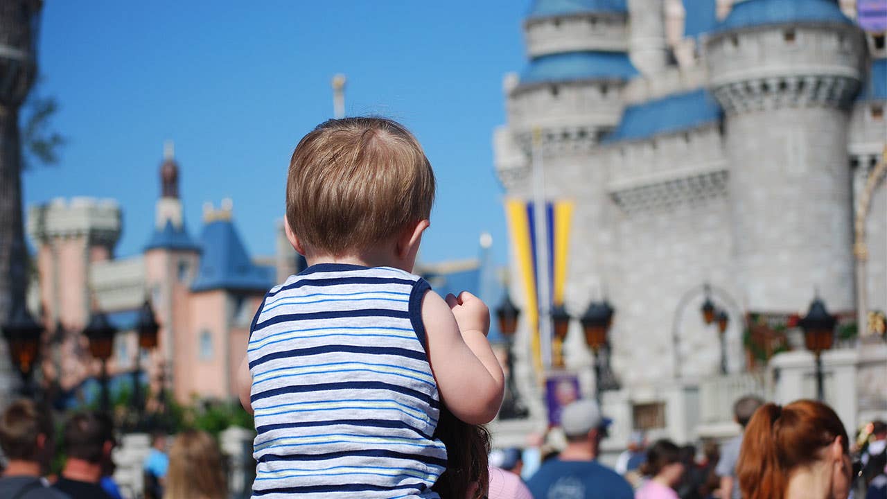Kid on parents shoulders in Disney World