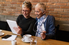 Woman and her older mother look together at tablet in cafe