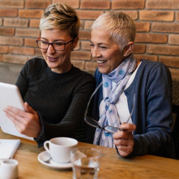 Woman and her older mother look together at tablet in cafe