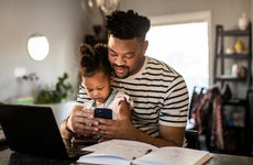 A father holds his daughter while looking at his phone