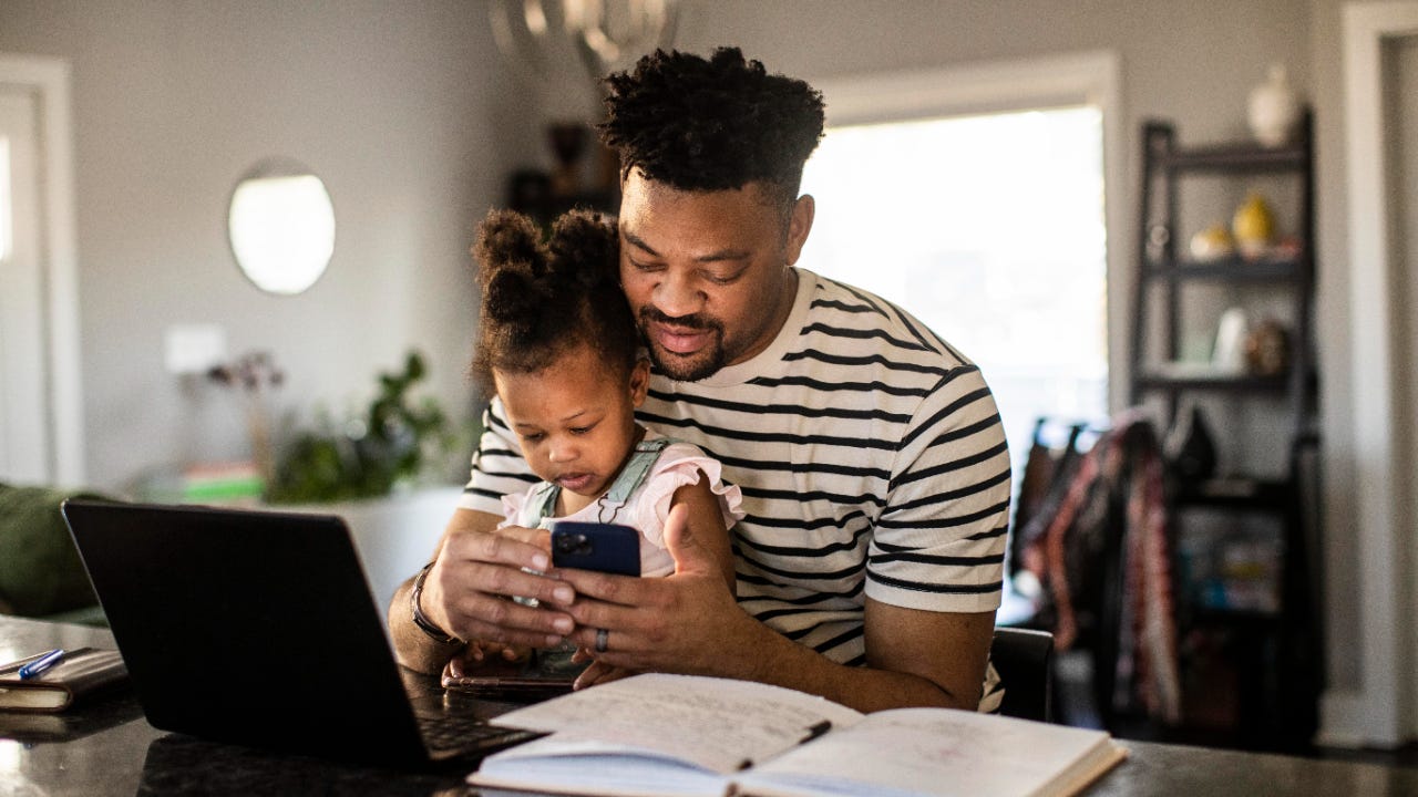 A father holds his daughter while looking at his phone