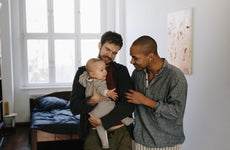 A gay couple stands in their home, interacting with their child.