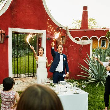 Man and woman holding sparklers to celebrate a wedding outside a red bark.