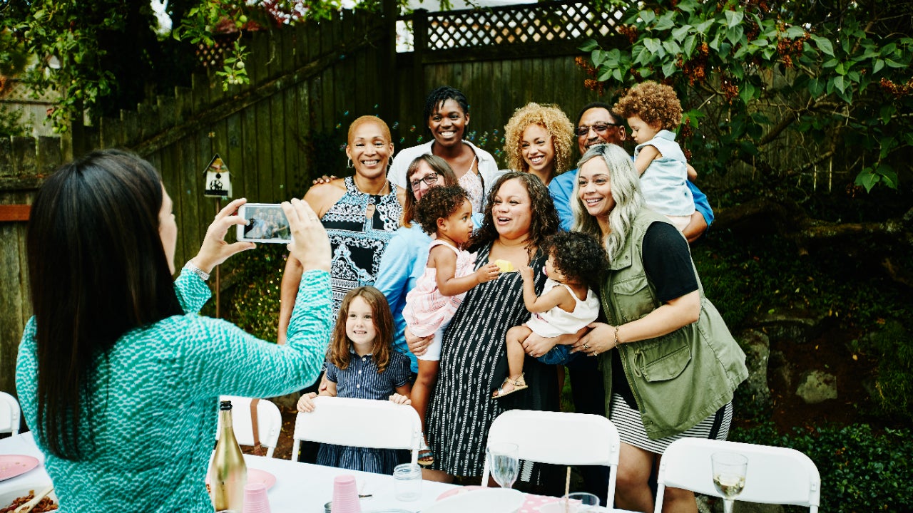 Woman taking photo with smartphone of smiling multi-generation family at backyard birthday party