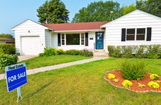 white suburban house with green front yard and landscaping, for sale sign out front