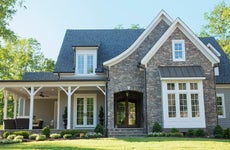 Front of a stone suburban home with a white front porch and green lawn