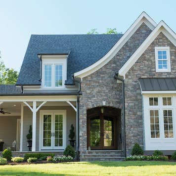 Front of a stone suburban home with a white front porch and green lawn