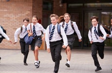 A group of private school children in uniform dashes in front of a school