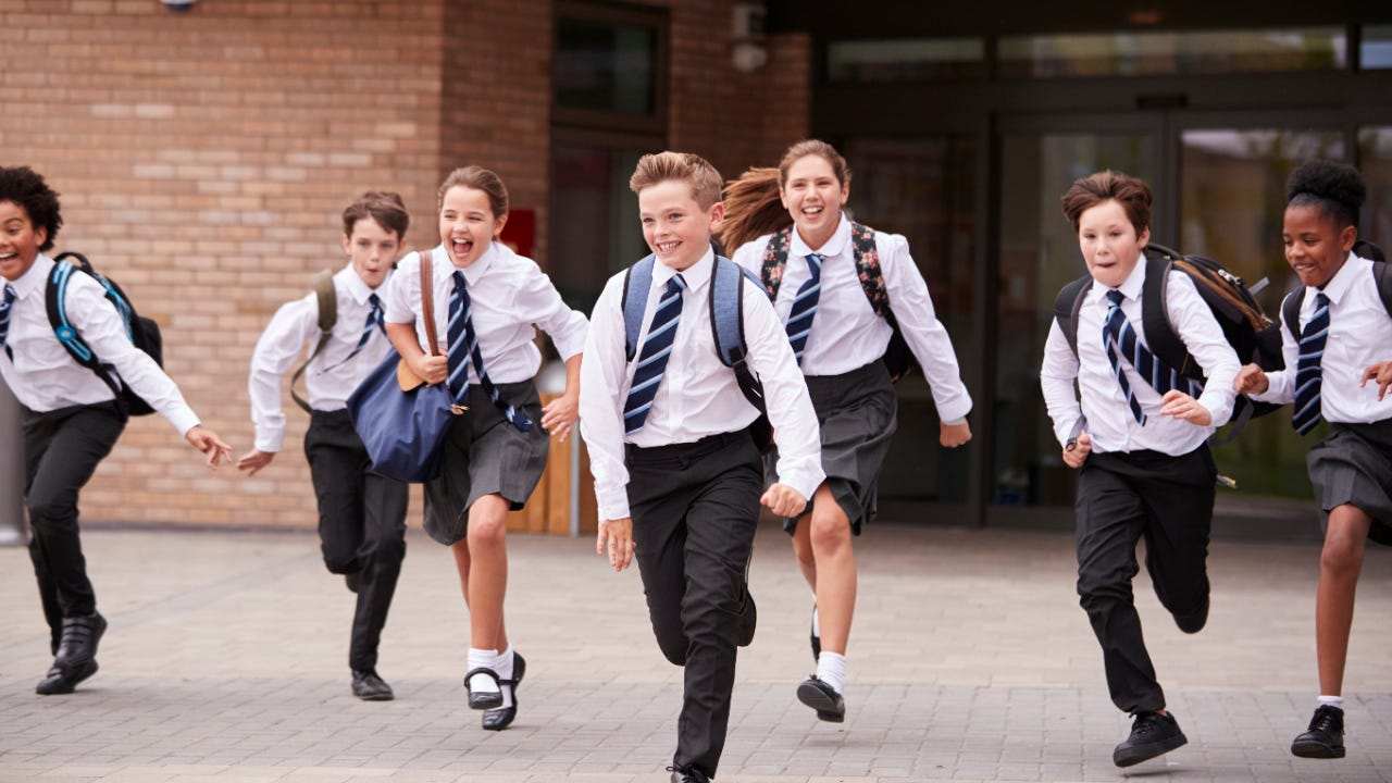 A group of private school children in uniform dashes in front of a school