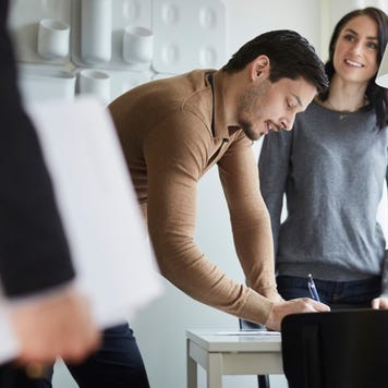 A man signing a contract as his wife looks on.