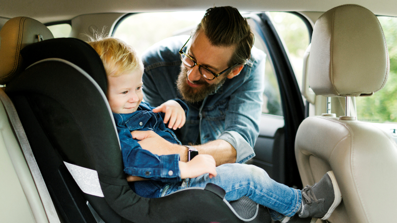man buckling his son into his car seat