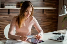 Woman at desk looking at tablet with credit card
