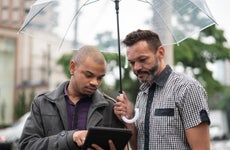 Two people under umbrella using tablet
