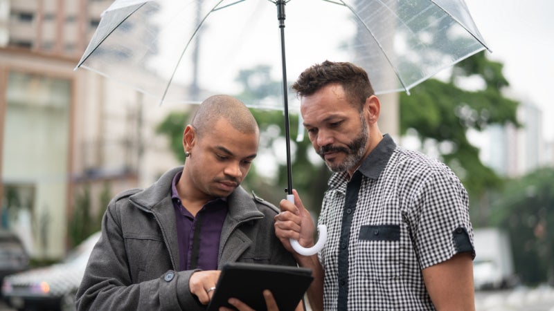 Two people under umbrella using tablet
