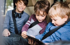 three boys looking at a tablet in the back seat of a car
