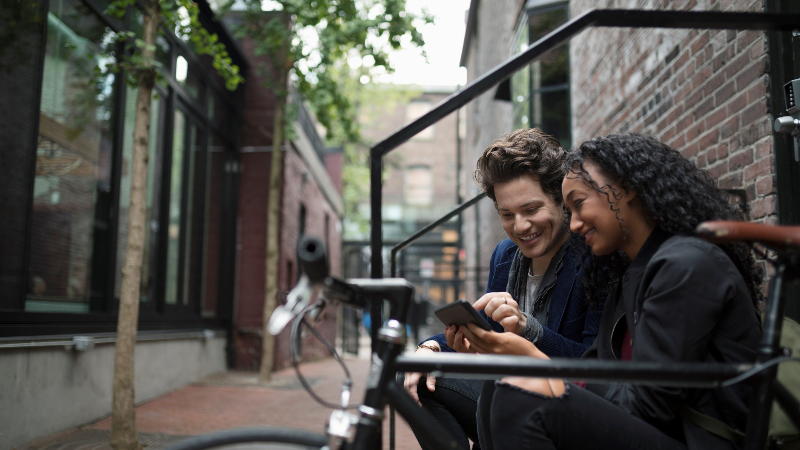 Young couple texting with smart phone on urban stoop
