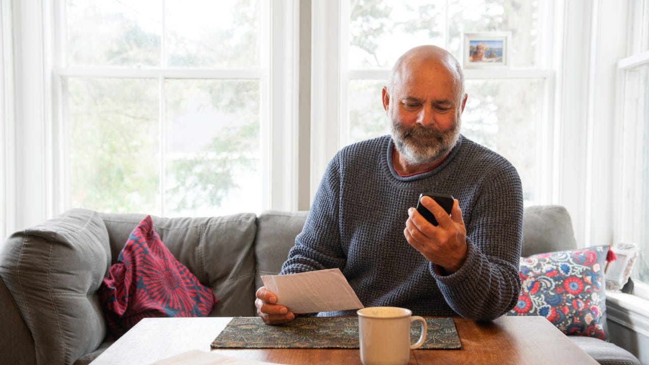 A mature, mixed race man dealing with finances and bills at home in his dining room. Photographed in North America