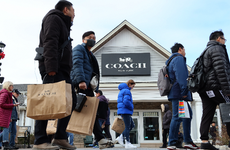 Consumers walking past a Coach store with shopping bags.