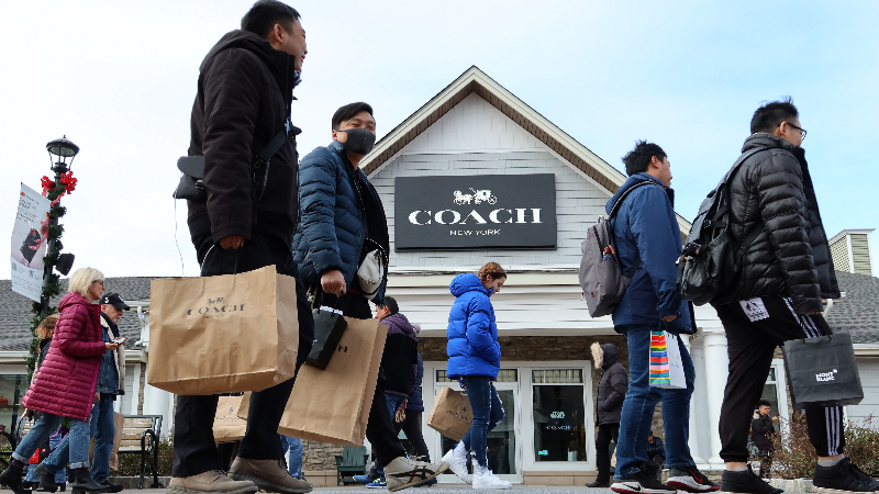Consumers walking past a Coach store with shopping bags.