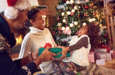 family around the christmas tree while parents hand gift to daughter