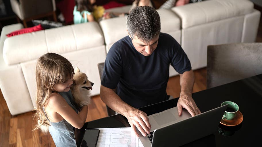 Girl holding small dog talking to father while he is working at home