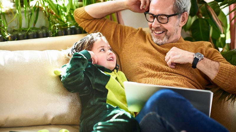 A middle age man plays with his granddaughter on the couch